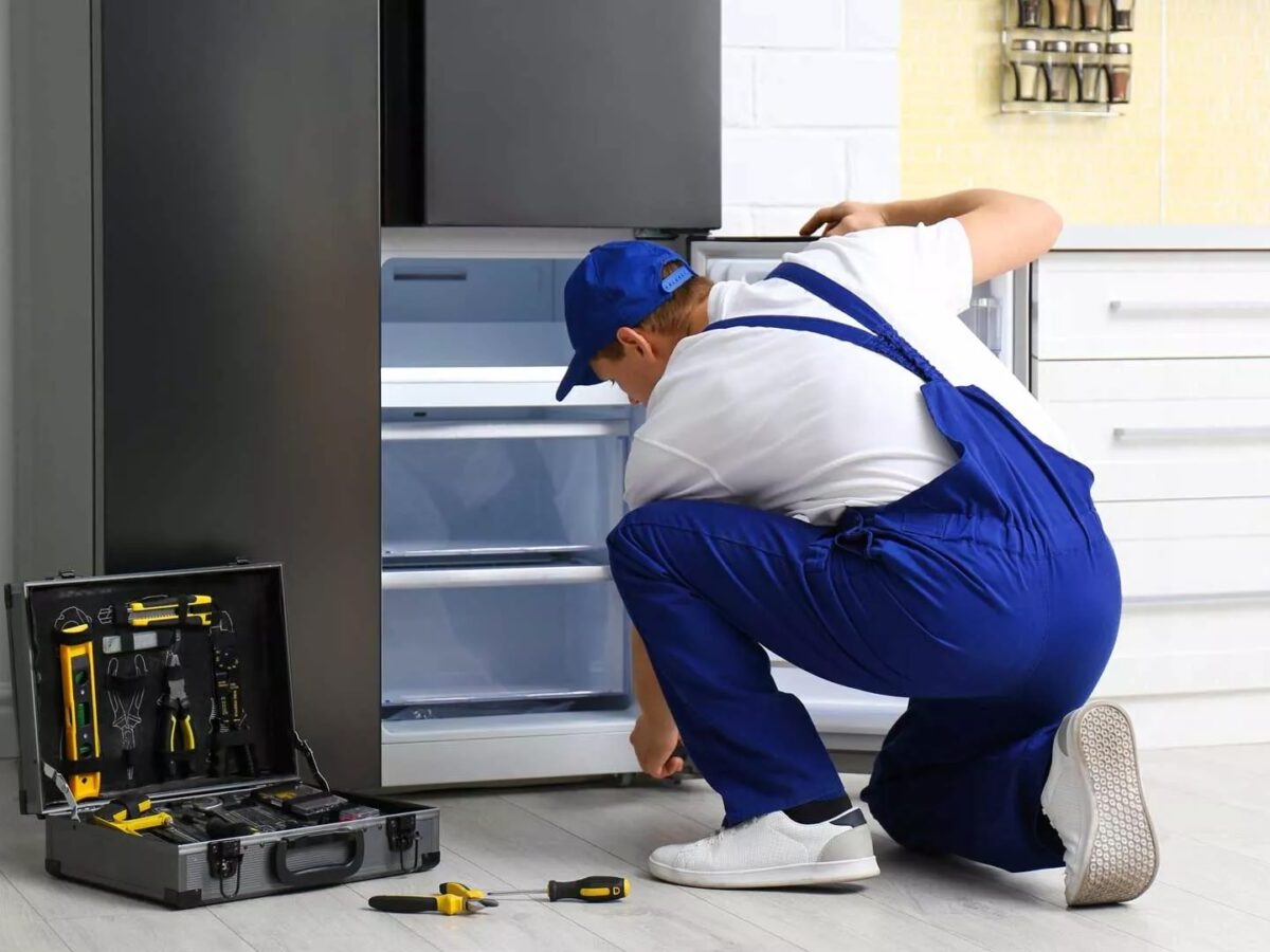 Técnico reparando nevera con puerta abierta y herramientas